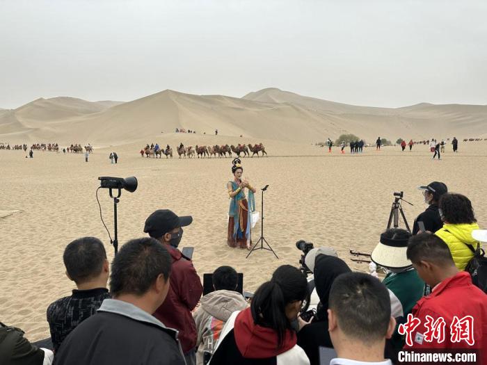 圖為2023年4月底，敦煌大漠“逐舞者”奧楠在鳴沙山月牙泉景區(qū)視頻直播，吸引游人圍觀?！●T志軍 攝